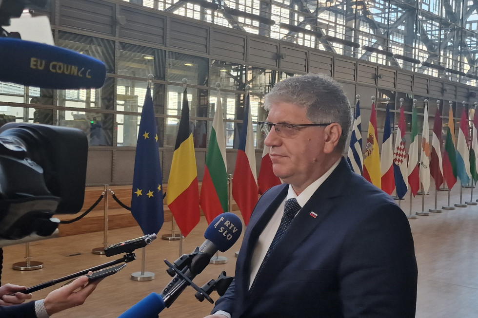 A bust of the Minister, with microphones in front of him, cameras to his left and several flags behind him.