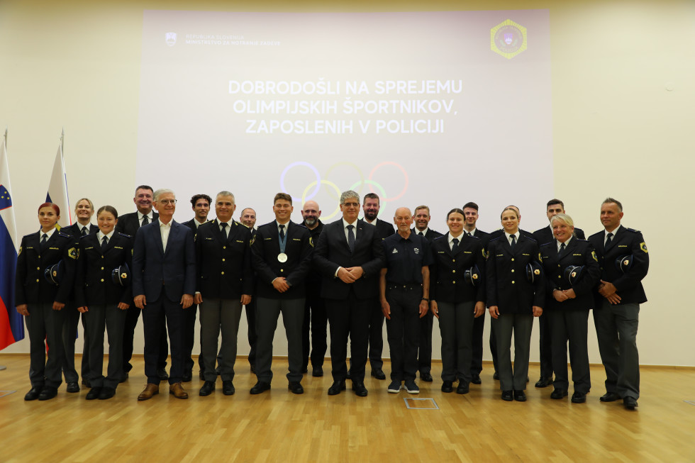 Skupinska fotografija na kateri pred steno stojijo sodelujoči, za njimi je na steni projekcija predstavitve