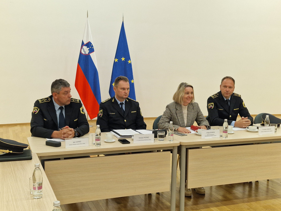 Sedijo v dvorani za svetlo rjavo leseno mizo. Za njimi je svetla stena ter slovenska in evropska zastava.