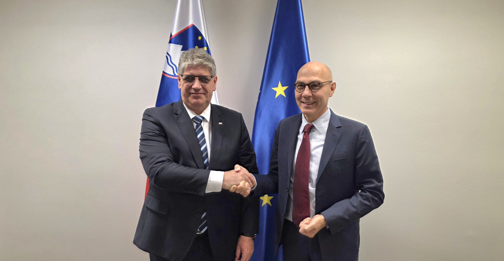 Minister in komisar se rokujeta, za njima sta slovenska in evropska zastava