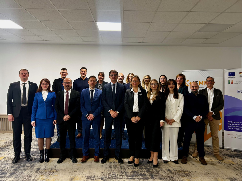 Udeleženci stojijo in se fotografirajo. Za njimi je stena bele barve, tla so rjavo-sive barve.