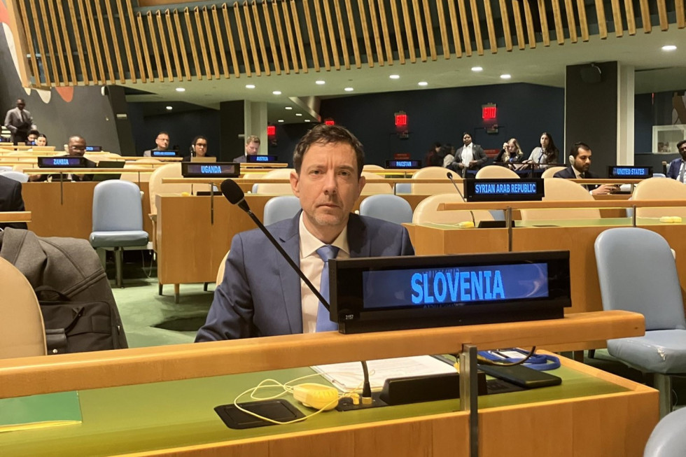 Sedi za delegatsko mizo v dvorani. Pred njim je na ekranu napis Slovenia..