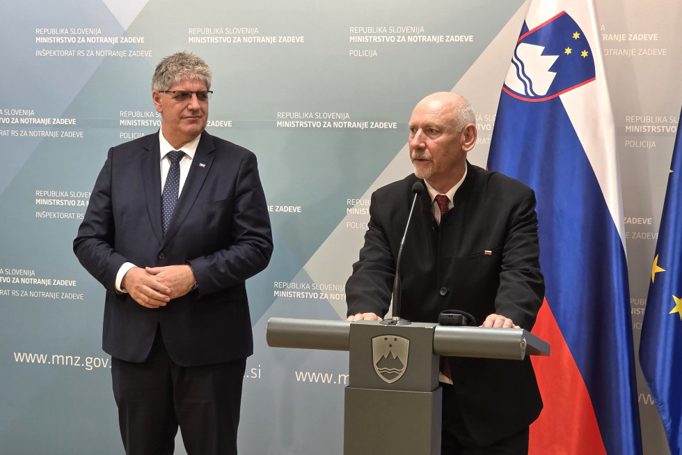 Minister stoji za govornico in govori, ob njem stoji dosedanji minister, za njima ob modri steni z napisom ministrstva sta slovenska in evropska zastava