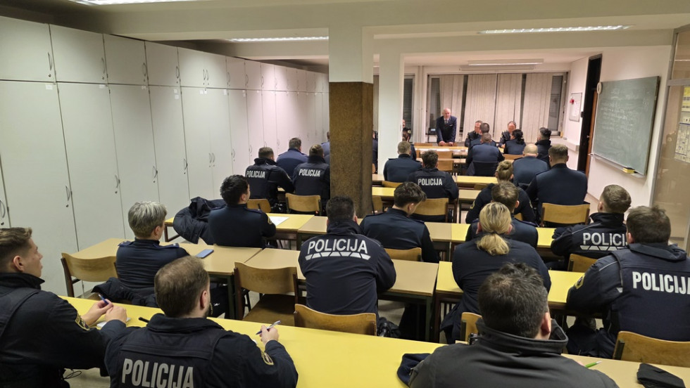 Policisti sedijo za mizami. Pred njimi stoji minister in jim govori.