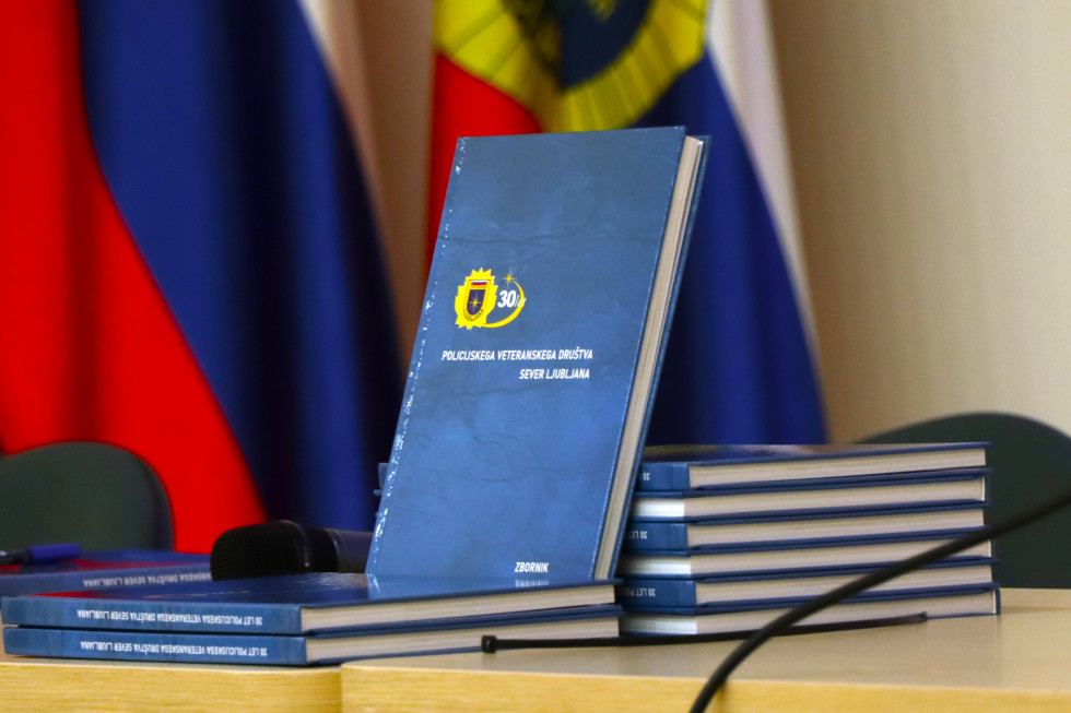 Pogled na knjigo, ki je postavljena na mizo. Platnica je modre barve z grbom v rumeni barvi. V ozadju je vidna policijska zastava.