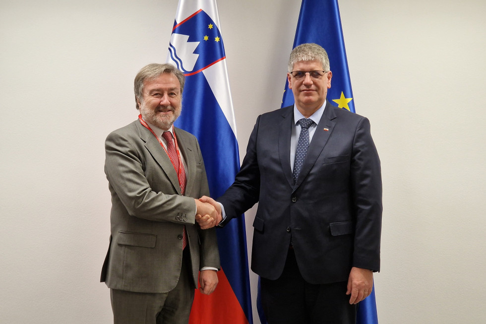 Minister in veleposlanik se rokujeta, za njima sta slovenska in evropska zastava