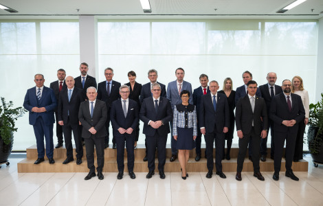 Skupinska fotografija  (Participants stand side by side in two rows, with white tiles on the floor and white ties behind them in front of a glass wall.)