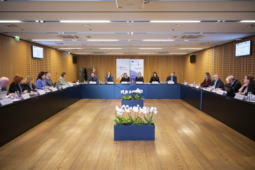Conference room, U-shaped tables with people sitting behind them. Flooring: parquet and flower arrangement.