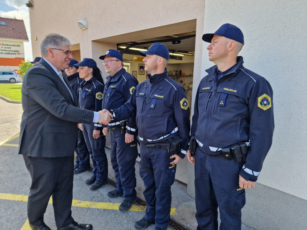 Policistke in policisti stojijo na asfaltu pred zgradbo in se rokujejo z ministrom.