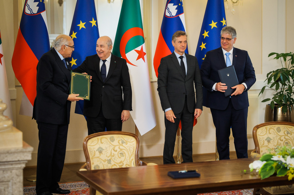 Štiri osebe stojijo, za njimi se vidijo zastave Alžirije, Slovenije in Evropske unije.