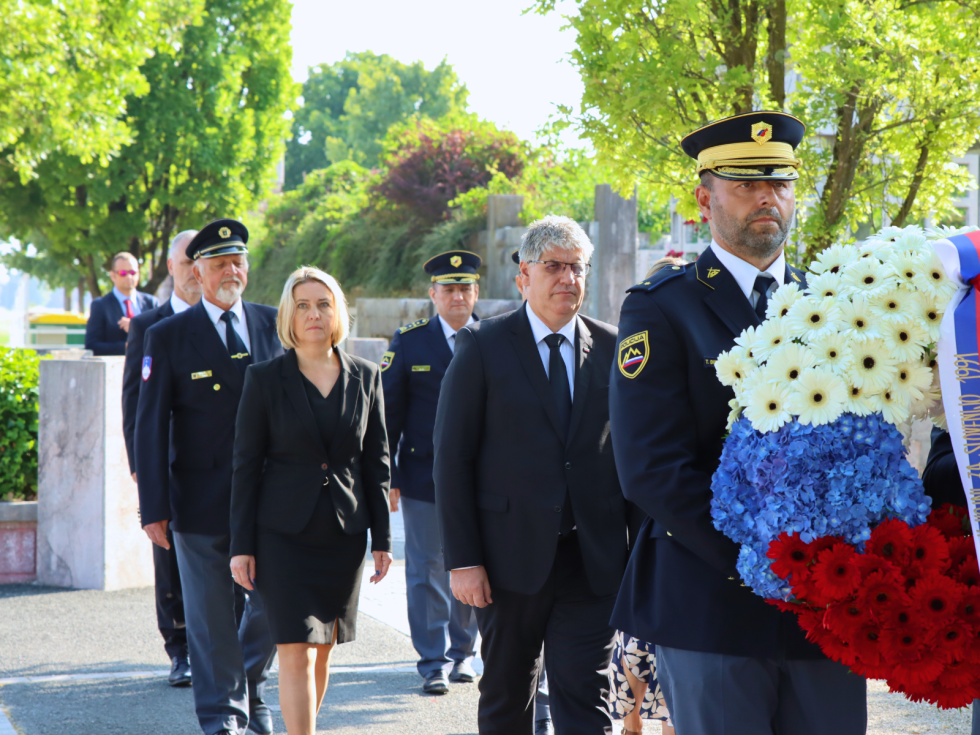 Delegacija hodi, pred njimi policista neseta venec v barvah slovenske zastave