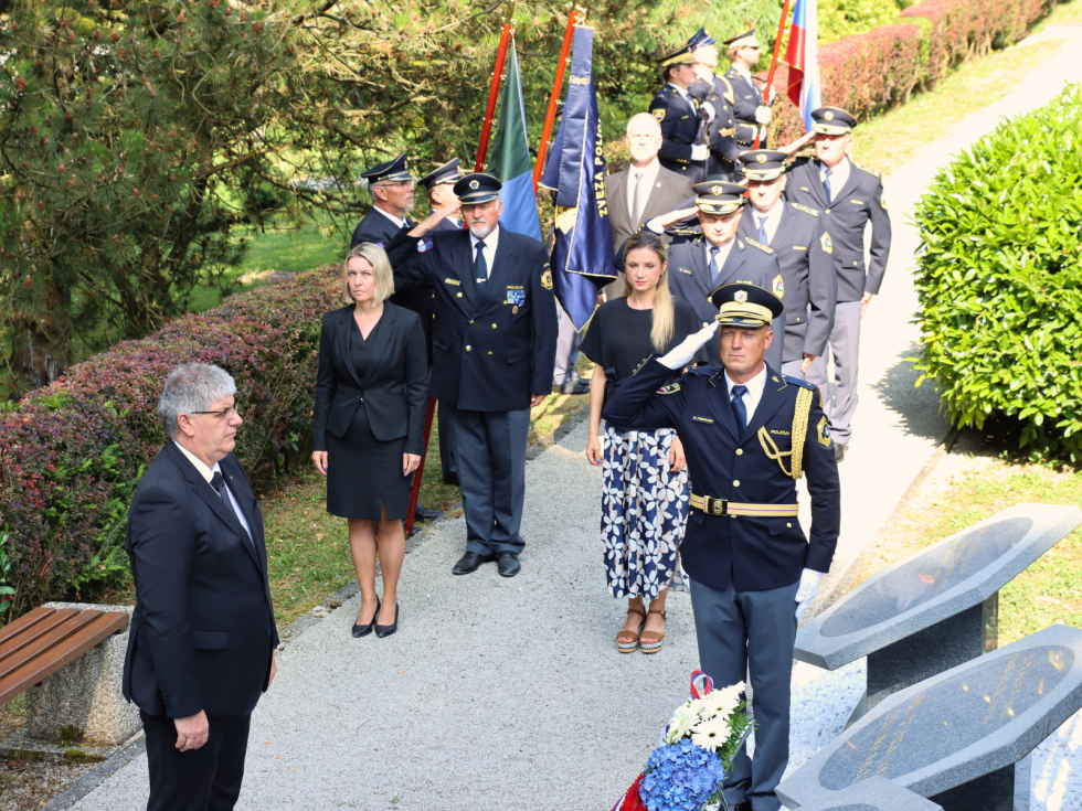 Delegacija stoji pred spomenikom, pred njim je venec v barvah slovenske zastave, ob robu stojijo praporščaki