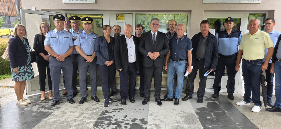 Udeleženci stojijo pred belo stavbo z okni.