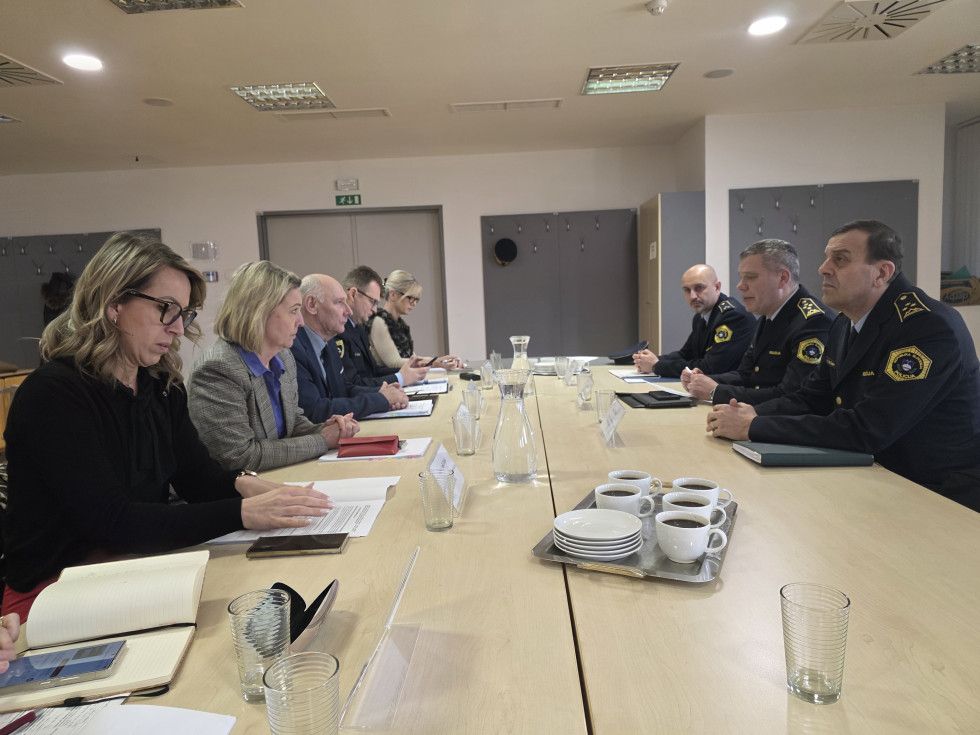 Udeleženci sedijo za bež mizo drug nasproti drugega in se pogovarjajo.