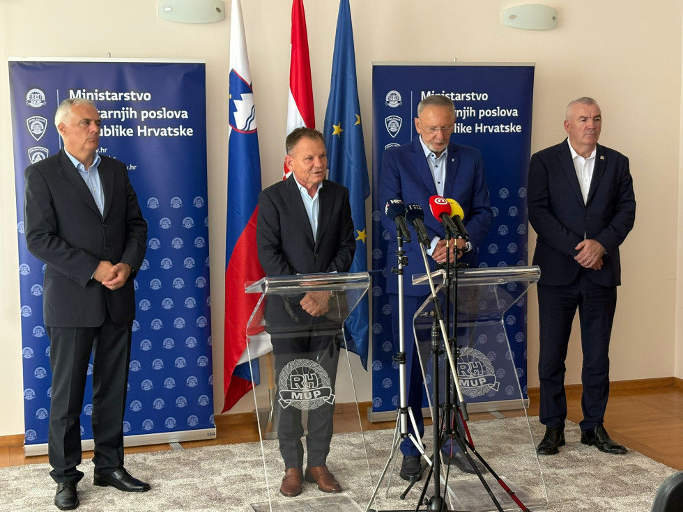 Ministra stojita za govornicama, ki sta iz pleksi materiala. Za njima sta dva modra panoja, na katerem piše Ministrstvo za notranje zadeve Republike Hrvaške, ter zastav Slovenije, Hrvaške in Evropske unije.