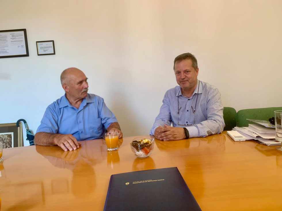 Državni sekretar Božo Predalič in načelnikk Upravne enote Kamnik sedita za sejno mizo med pogovorom.