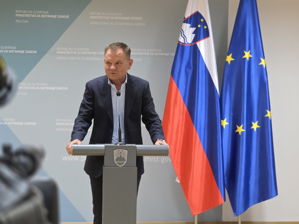 Minister stoji za sivo govornico in govori. Za njim je sivo ozadje ter zastavi Slovenije in Evropske unije.