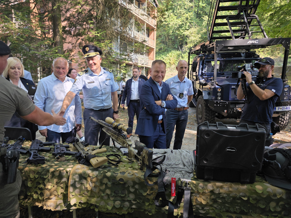 Oprema policije je razstavljena na mizah v parku, obiskovalci si jo ogledujejo.