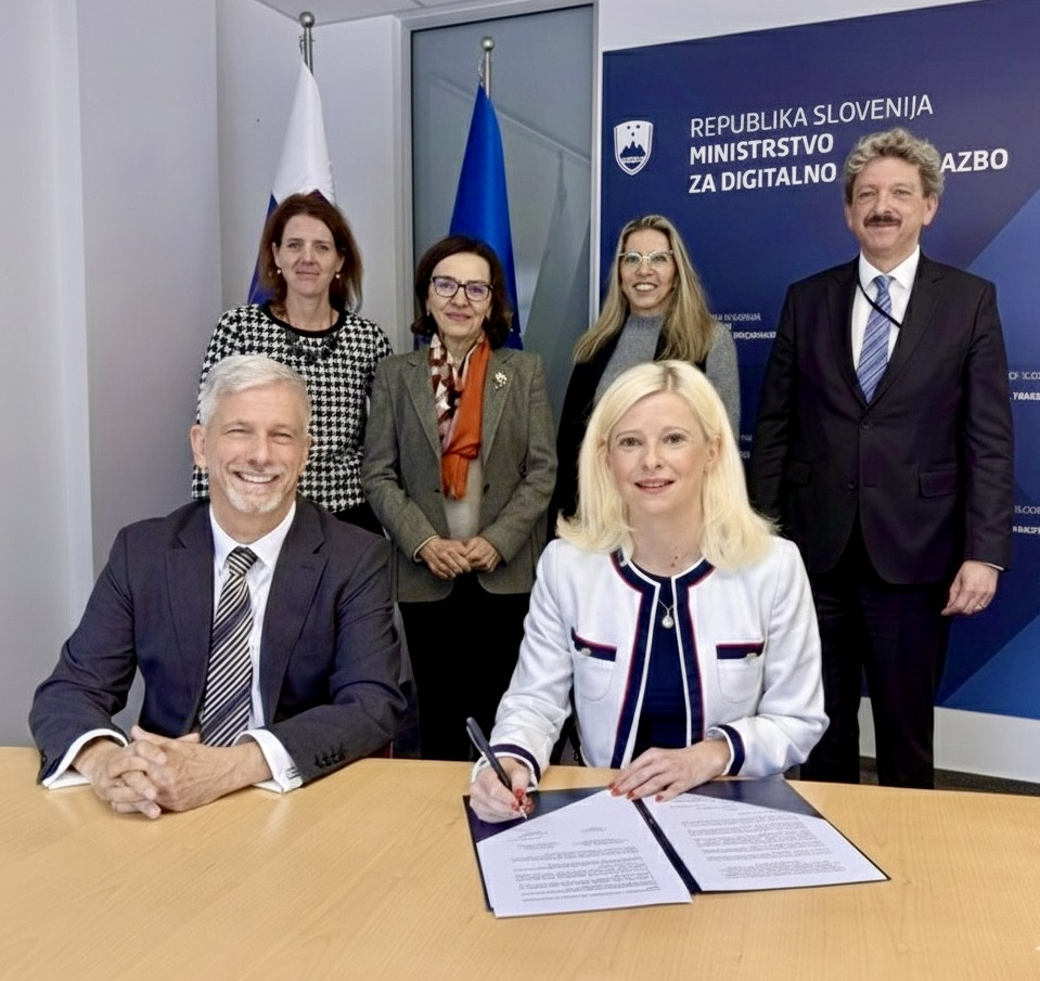 Ženska in moški sedita za mizo, ženska podpisuje dokument. 