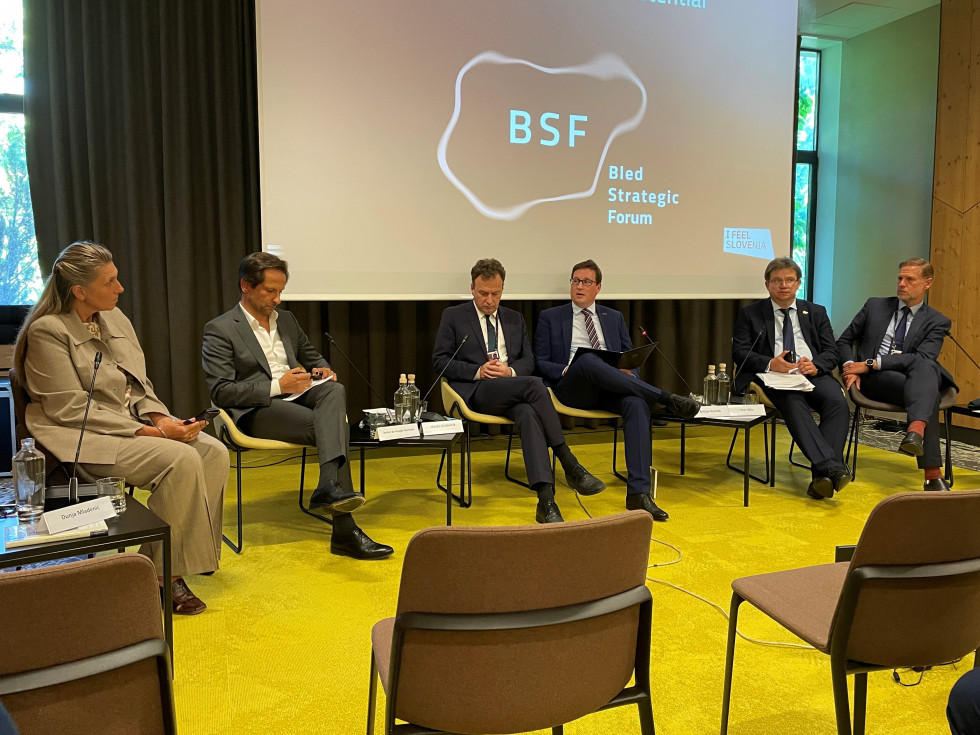 Udeleženci razprave, med njimi minister Koritnik, sedijo v ospredju dvorane, obrnjeni so proti publiki, v ozadju platno s projekcijo logotipa Blejskega strateškega foruma