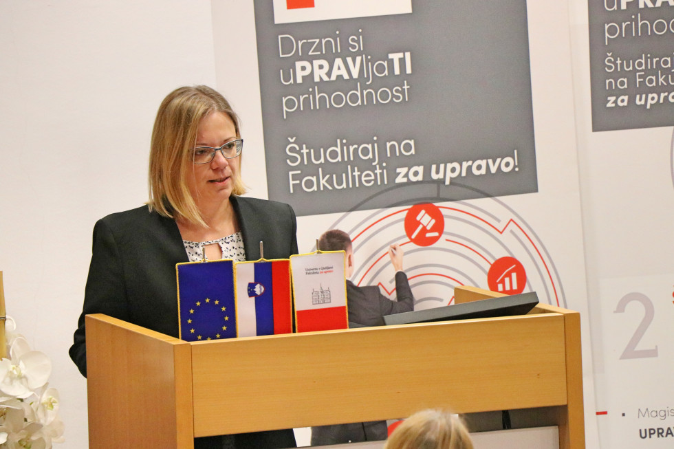 Ministrica stoji pred govorniškim pultom in nagovarja zbrane.
