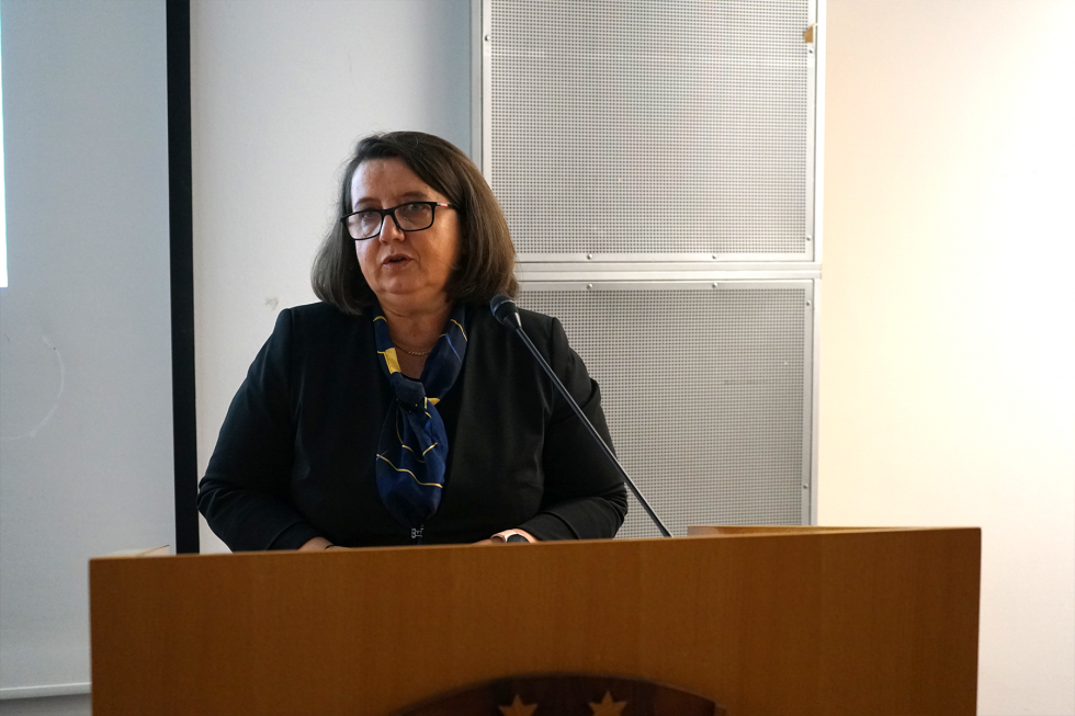 Državna sekretarka stoji za govorniškim odrom in ima nagovor.