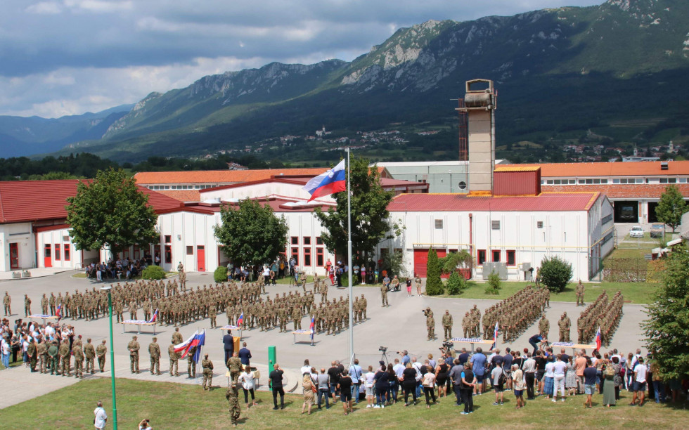 Udeleženci slovesnosti na prireditvenem prostoru, v ozadju vojašnica, gore in nebo z oblaki