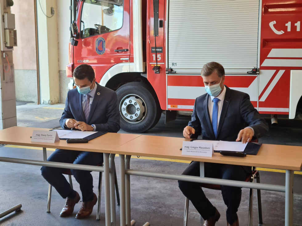 Minister in župan podpisujeta dokument za mizo, pred gasilskim avtomobilom