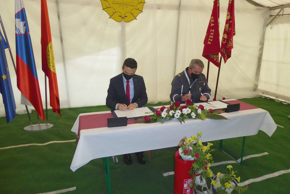 Minister in predsednik GZS podpisujeta pogodbo za mizo s cvetjem in zastavami Slovenije ter gasilskih združenj v ozadju