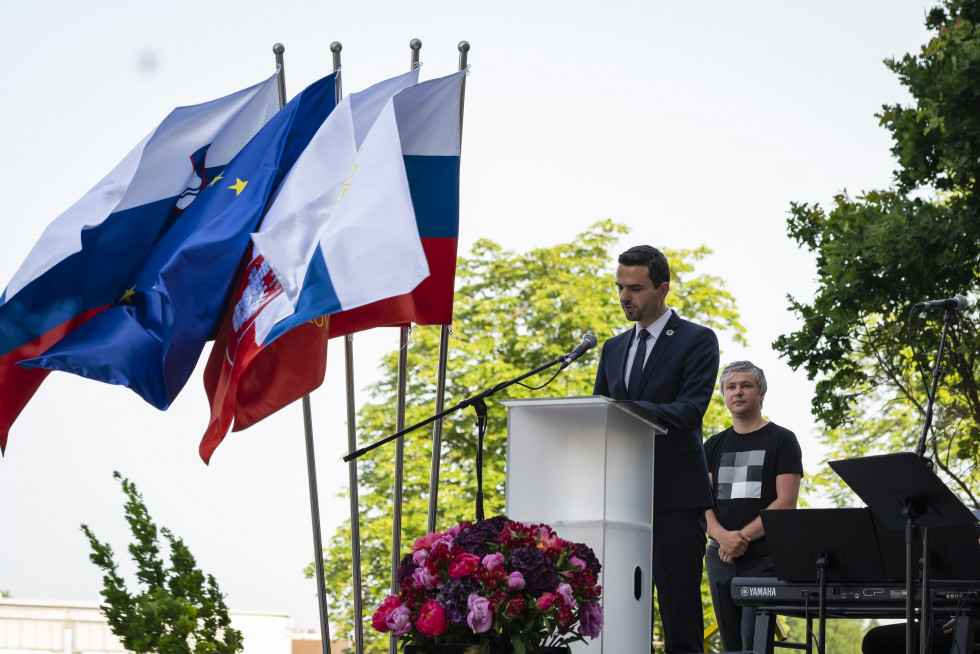 Minister za govornico pred plapolajočimi zastavami Slovenije, EU in mariborske občine