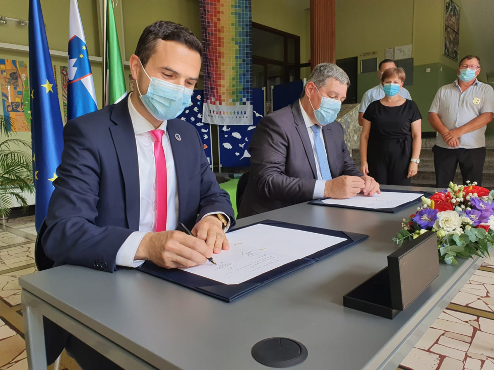 Minister in župan podpisujeta dogovor. V ozadju so zastave Slovenije, EU in občinska zastava