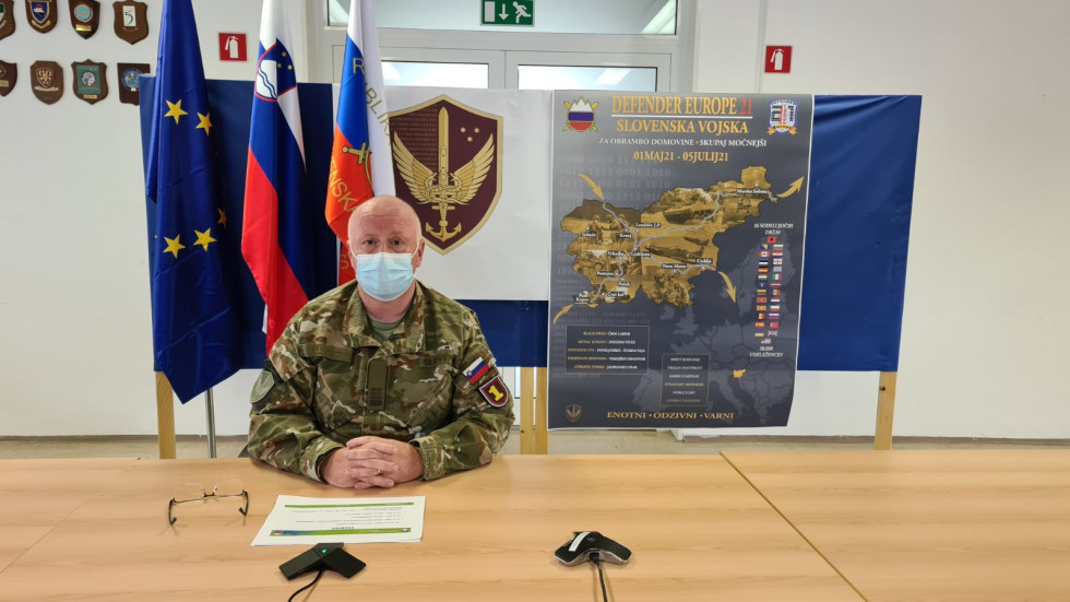 Načelnik Sektorja za usposabljanje na Poveljstvu sil Slovenske vojske sedi za mizo pred zastavami EU, Slovenije in Slovenske vojske ter plakatom vaje