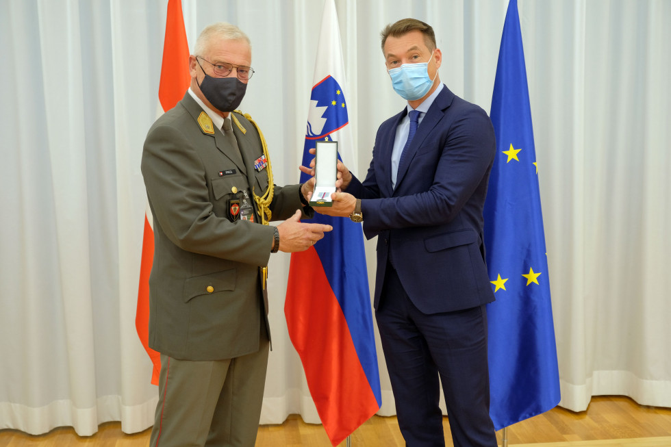 Sekretar in brigadir z medaljo. V ozadju zastave Avstrije, Slovenije in EU