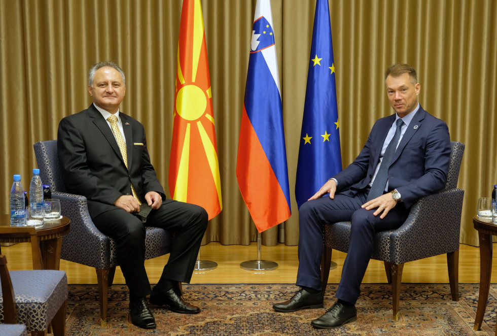 Sekretarja sedita v sejni sobi pred začetkom pogovorov. V ozadju so zastave Severne Makedonije, Slovenije in EUo