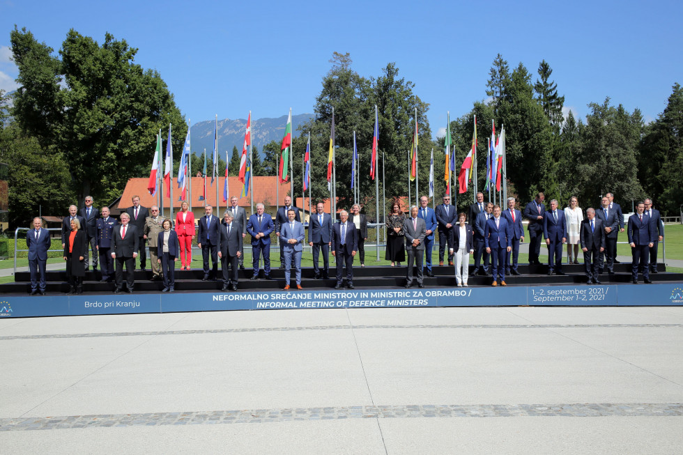 Ministri in drugi udeleženci zasedanja na stopnicah pred zastavami članic EU. V ozadju drevesa in gore v daljavi