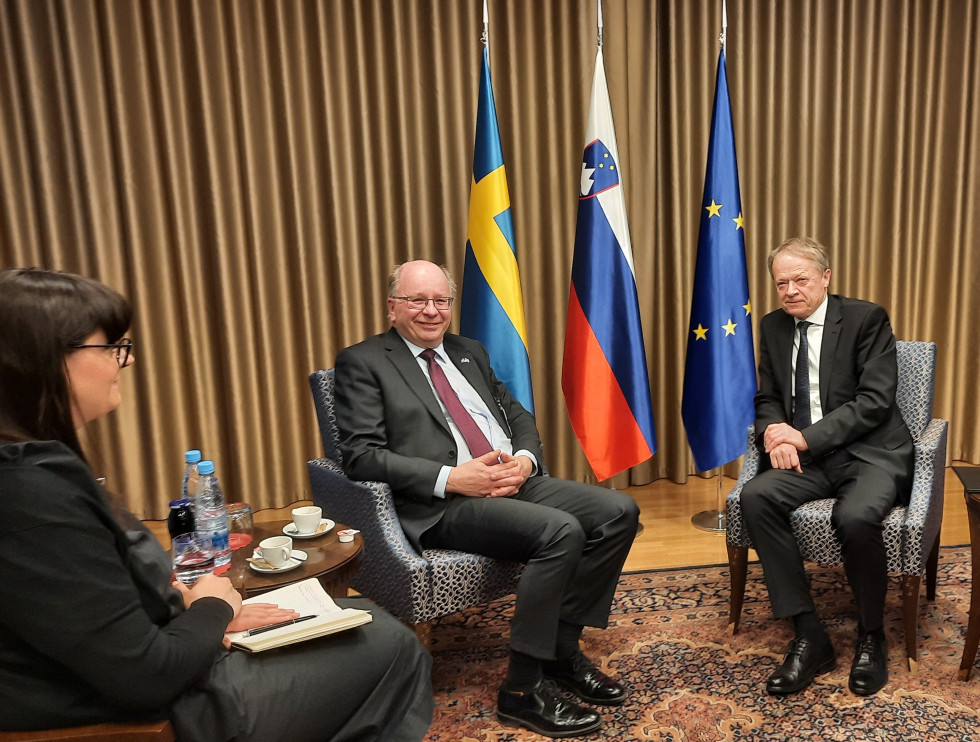 Sekretar in veleposlanik sedita v sprejemnici med pogovori. Zadaj so zastave Švedske, Slovenije in EU