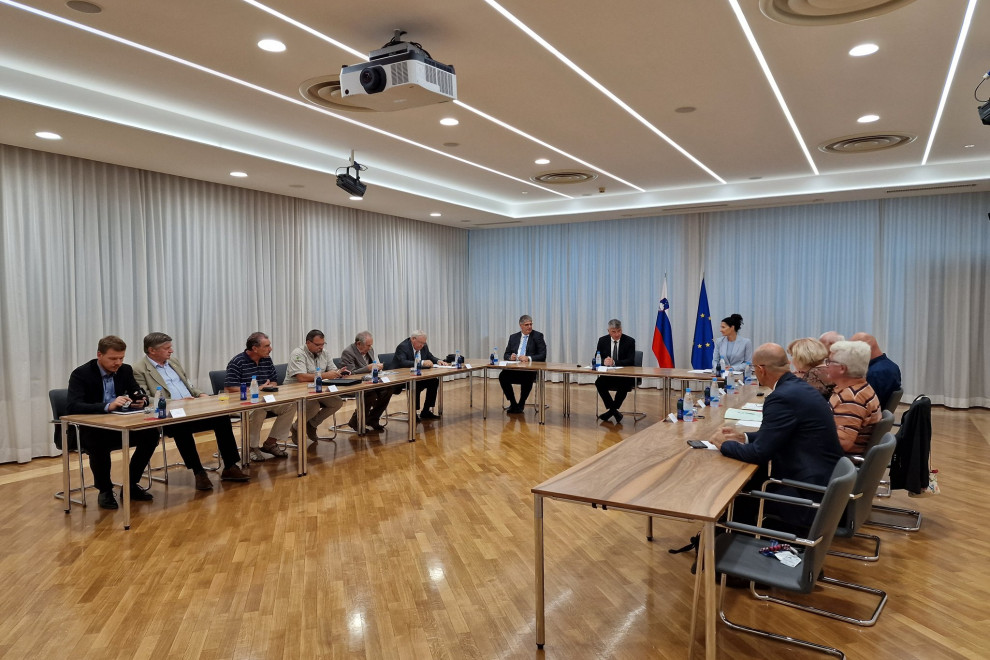 Udeleženci sestanka sedijo za mizami v veliki dvorani ministrstva