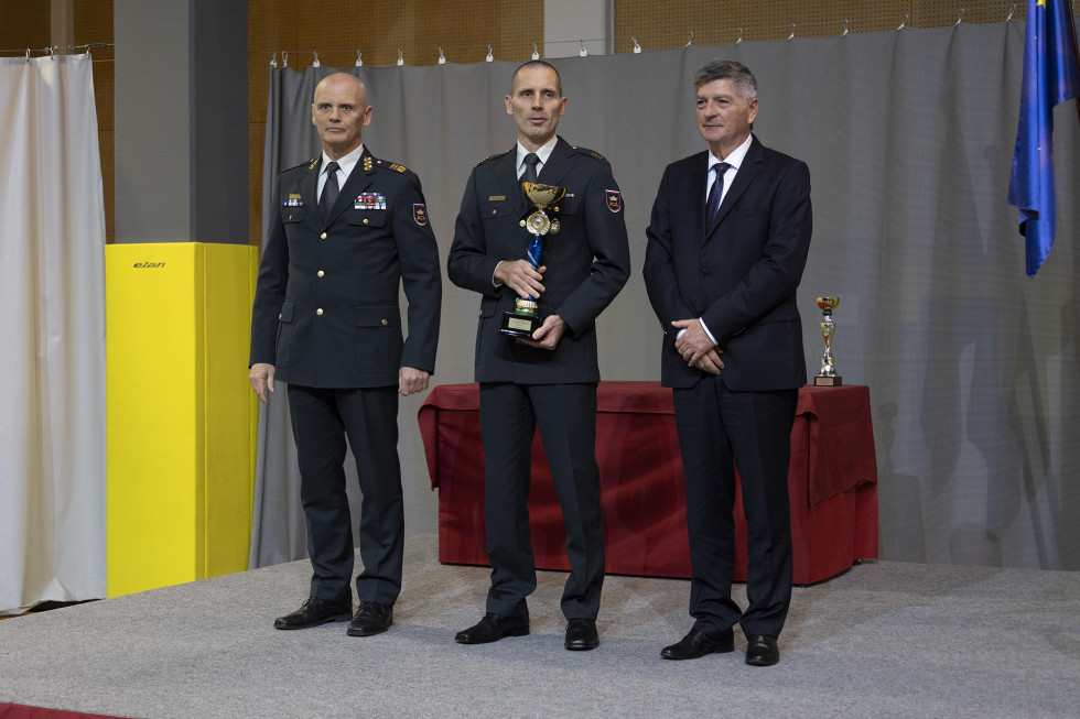 Športnik leta Slovenske vojske s pokalom v rokah stoji na odru s sekretarjem in načelnikom