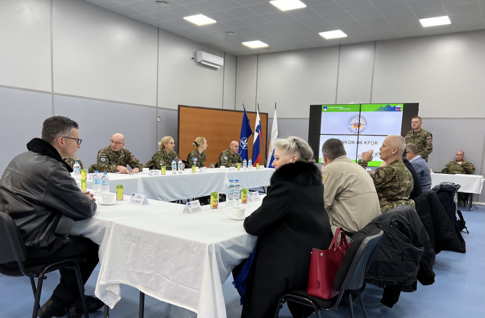 Delegacija ministrstva sedi s predstavniki kontingenta Slovenske vojske za sejno mizo. Zadaj je platno s projekcijo