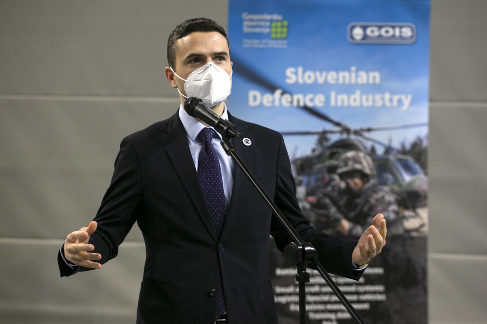 Minister stoji pred mikrofonom. V ozadju je plakat predstavitve slovenske obrambne industrije