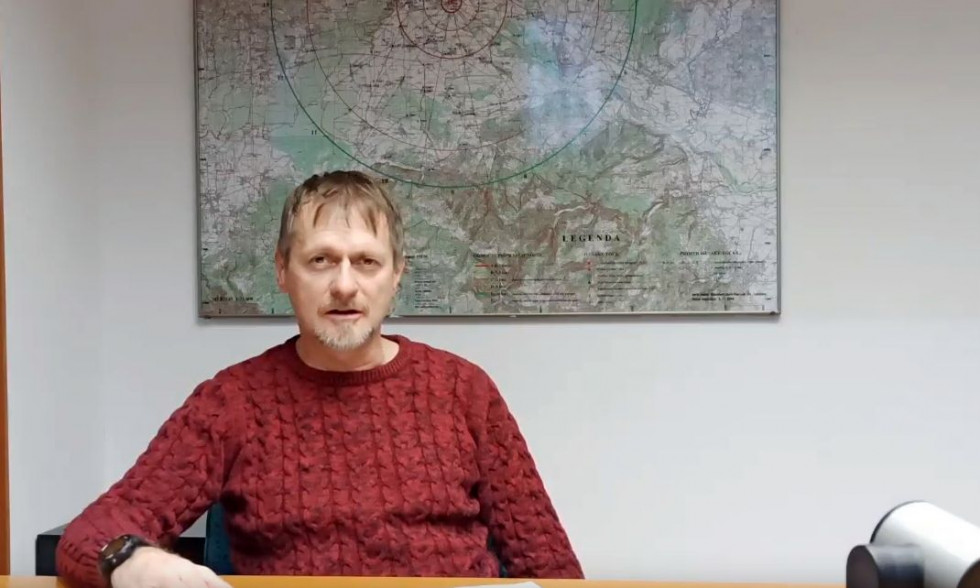 Boštjan Tavčar sedi pred kamero med video konferenco. V ozadju je na steni zemljevid Slovenije