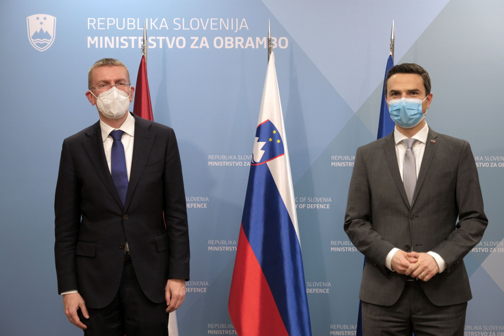 Ministra pred začetkom srečanja stojita pred zastavami Latvije in Slovenije ter EU. Za njima je moder pano ministrstva.