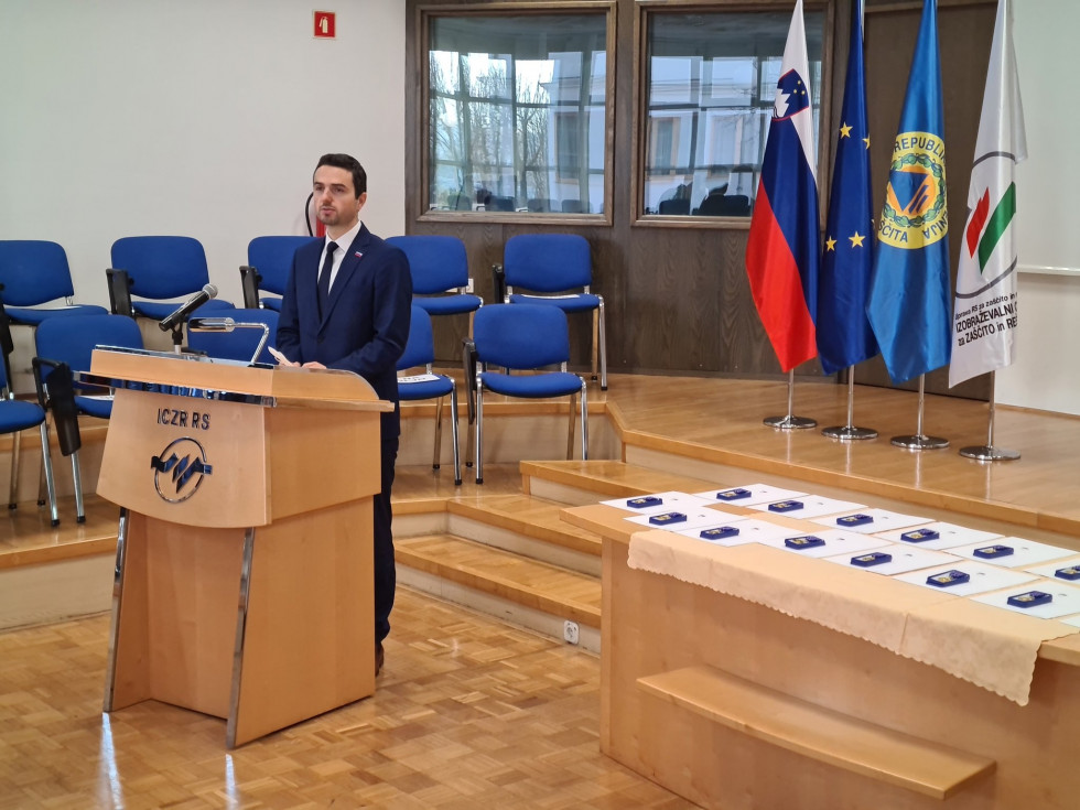 Minister za govornico. Ob njem je miza z medaljami.