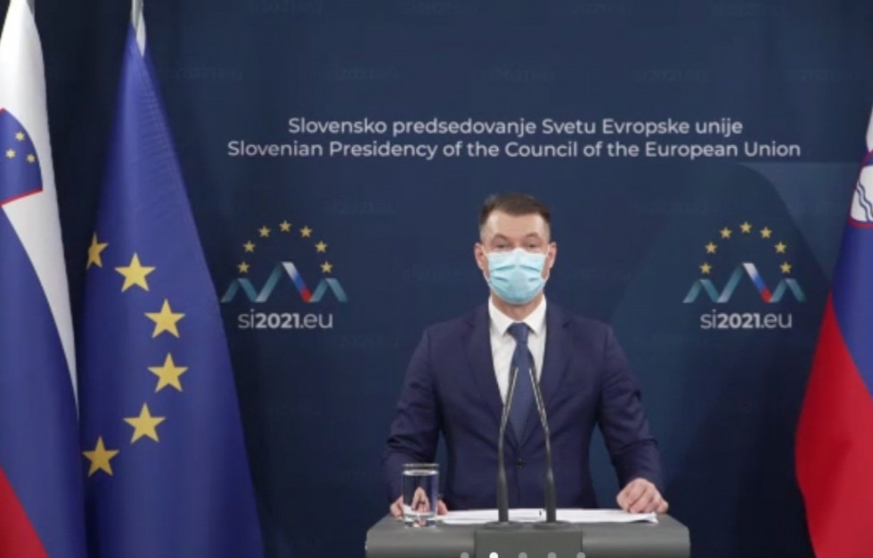 Sekretar stoji za govornico. Na obeh straneh sta zastavi Slovenije in EU, za njim pa pano predsedovanja