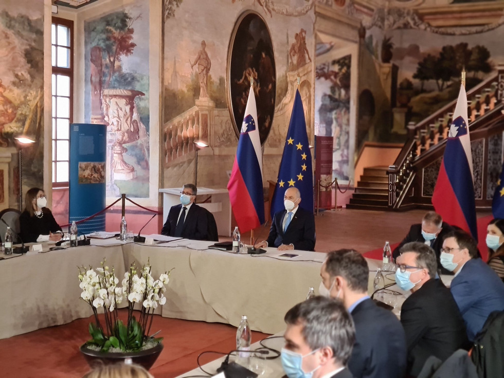 Člani vlade sedijo za veliko sejno mizo v bogato poslikani grajski dvorani