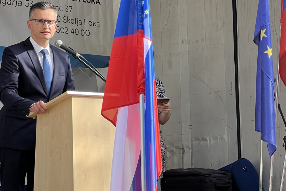Minister stoji za govornico. Pred njim sta zastavi Slovenije in EU