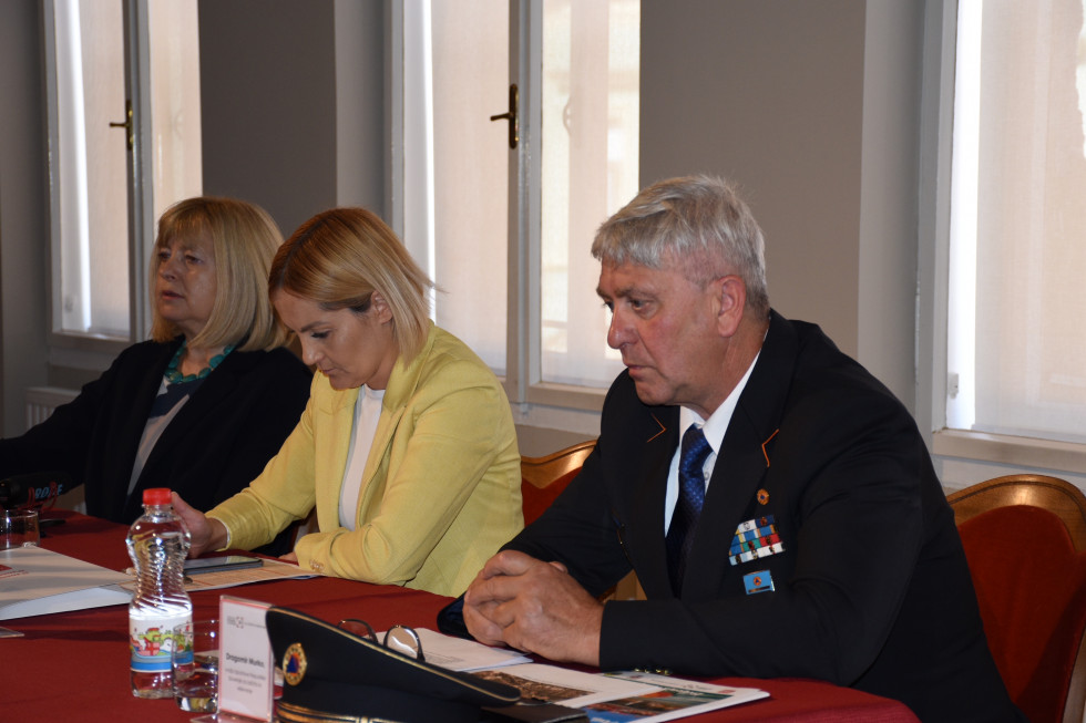 Udeleženci novinarske konference sedijo za mizo. Pred njimi so napisne tablice z imeni