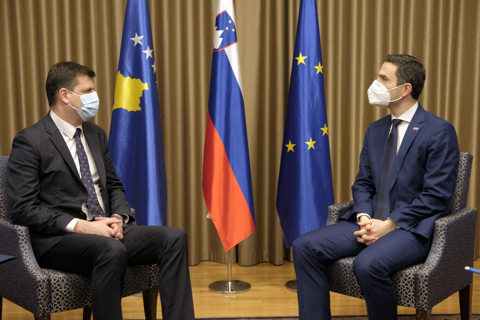 Minister in veleposlanik sedita v sprejemnici med pogovori. Za njima so zastave Kosova, Slovenije in EU