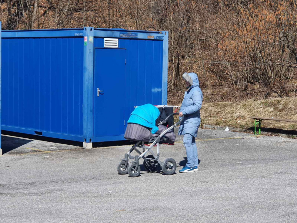 Begunka z otrokom v vozičku pred bivalnim kontejnerjem