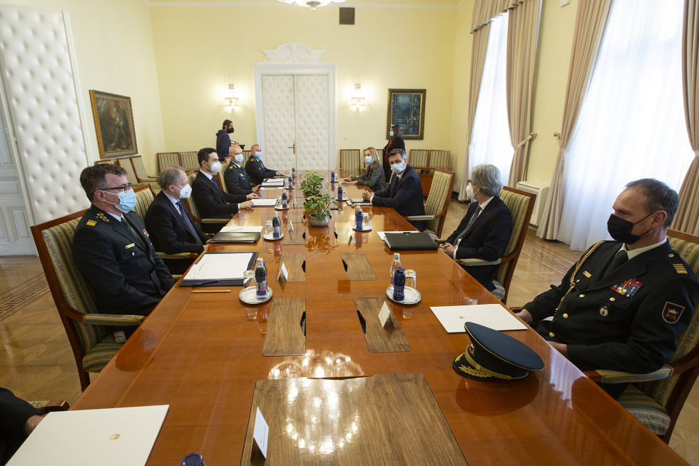 Predsednik, minister in načelnik s spremljevalci sedijo za sejno mizo. 